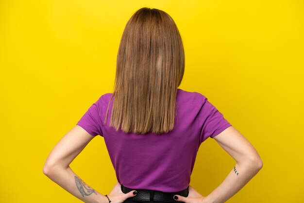 Young English woman isolated on yellow background in back position