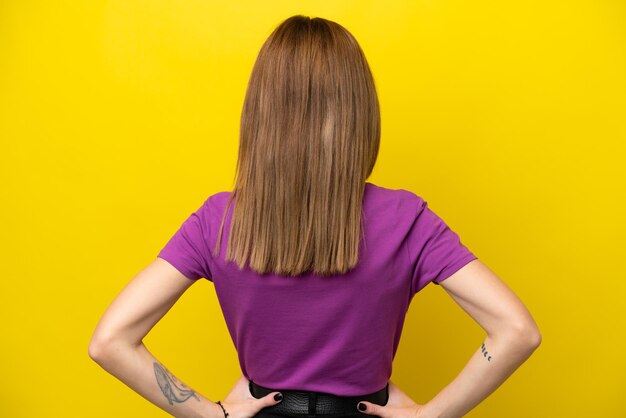 Young english woman isolated on yellow background in back\
position