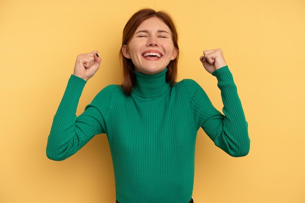 勝利の情熱と熱意の幸せな表現を祝う黄色の背景に分離された若いイギリス人女性