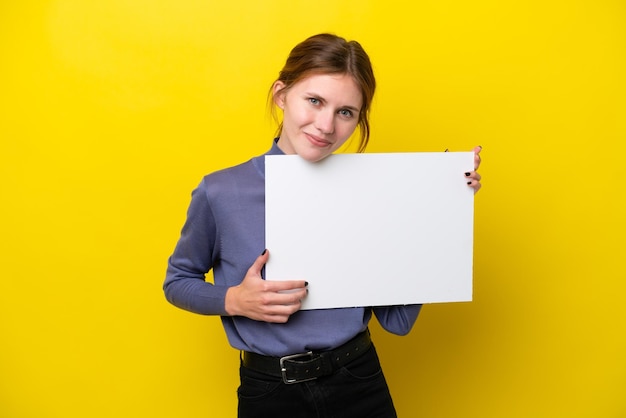 Young English woman isolated on yellow background holding an empty placard with happy expression