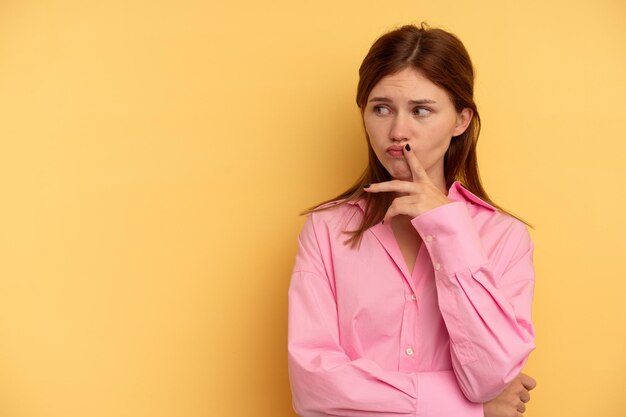 Young English woman isolated on yellow background looking sideways with doubtful and skeptical expression.