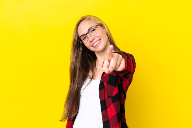 Young english woman isolated on yellow background pointing front with happy expression