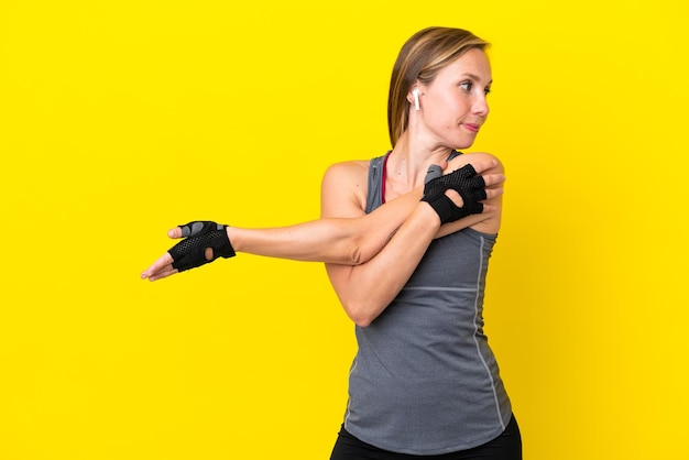 Young English woman isolated on yellow background stretching arm