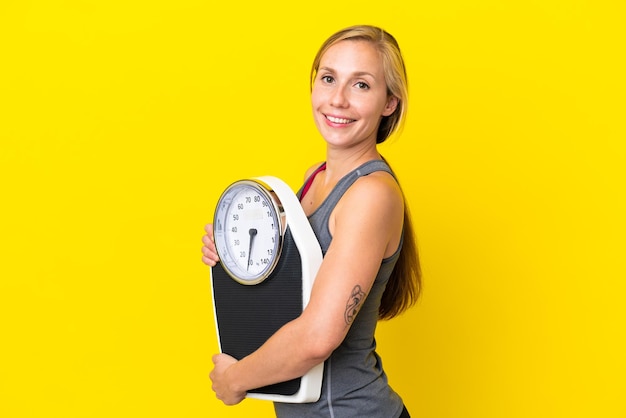 Young English woman isolated on yellow background with weighing machine