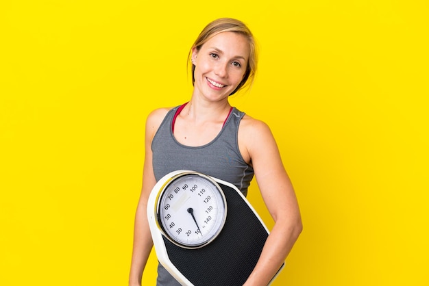 Young english woman isolated on yellow background with weighing machine