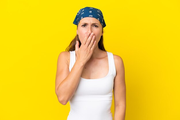 Young english woman isolated on yellow background yawning and covering wide open mouth with hand