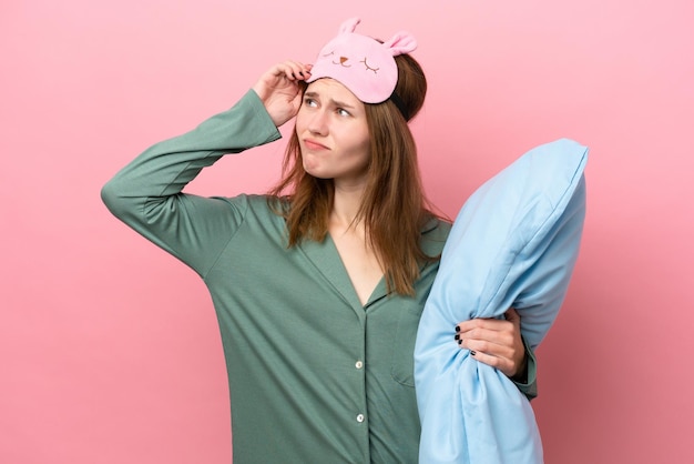 Young English woman in pajamas isolated on pink background in pajamas and having doubt with confuse face expression