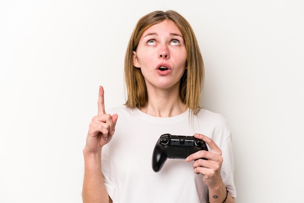 Young English woman playing with a video game controller isolated white background pointing upside with opened mouth