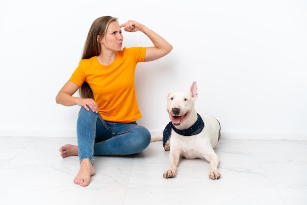 疑いを持って、混乱した表情で白い背景に隔離された彼女の犬と一緒に床に座っている若いイギリス人女性