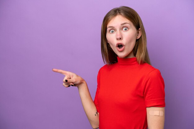 Young english woman wearing bandaids isolated on purple background surprised and pointing side