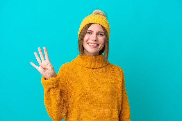 Молодая англичанка в зимней куртке на синем фоне счастлива и считает четыре пальцами
