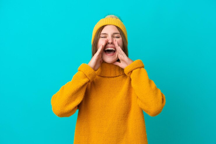 Фотография молодая англичанка в зимней куртке на синем фоне кричит и что-то объявляет