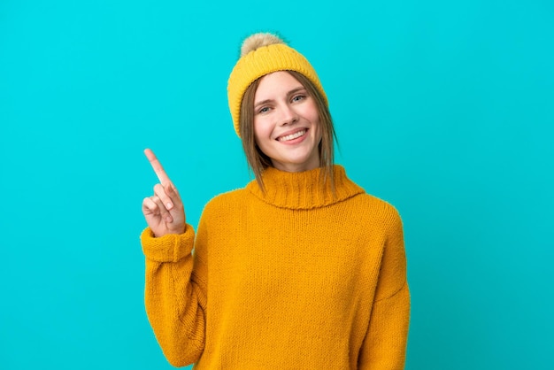 Young English woman wearing winter jacket isolated on blue background showing and lifting a finger in sign of the best