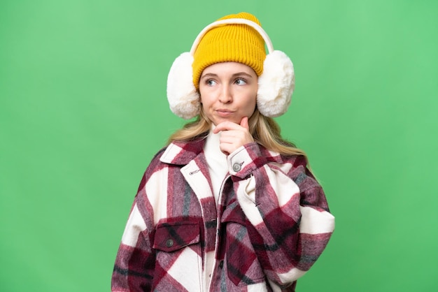 Young English woman wearing winter muffs over isolated background having doubts and with confuse face expression