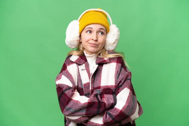 Young English woman wearing winter muffs over isolated background making doubts gesture while lifting the shoulders