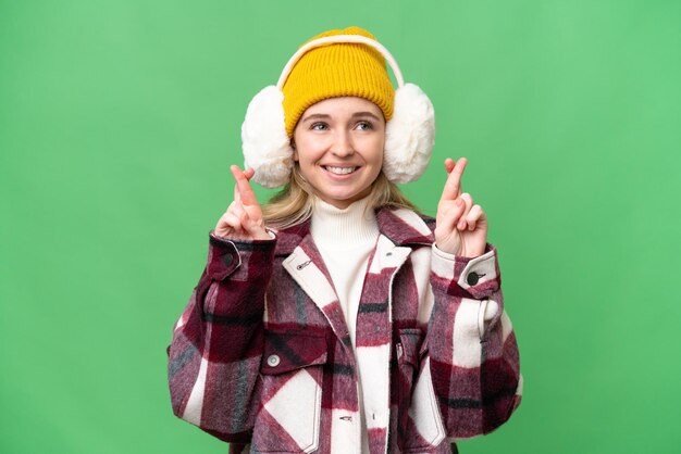 Photo young english woman wearing winter muffs over isolated background with fingers crossing