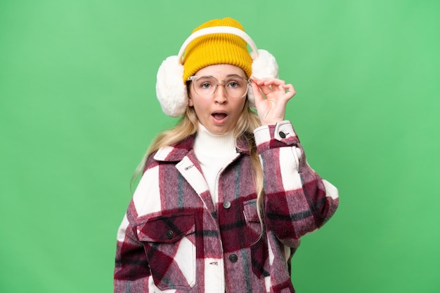 Photo young english woman wearing winter muffs over isolated background with glasses and surprised