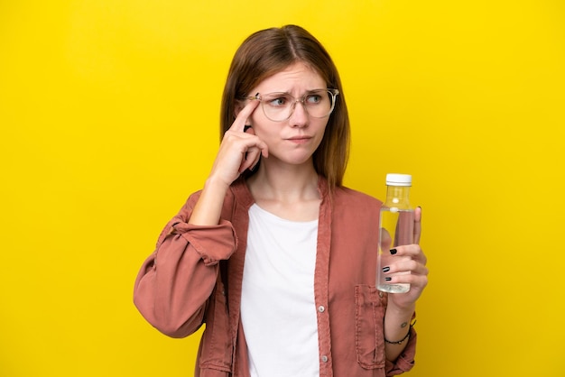 노란색 배경에 물 한 병을 들고 의심하고 생각하는 젊은 영국 여성
