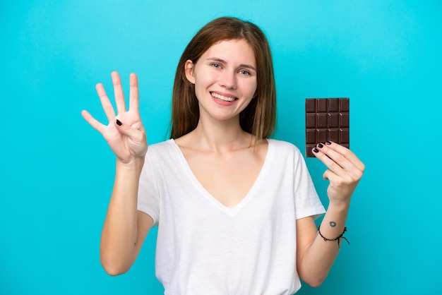 Молодая англичанка с шоколадом на синем фоне счастлива и считает четыре пальцами