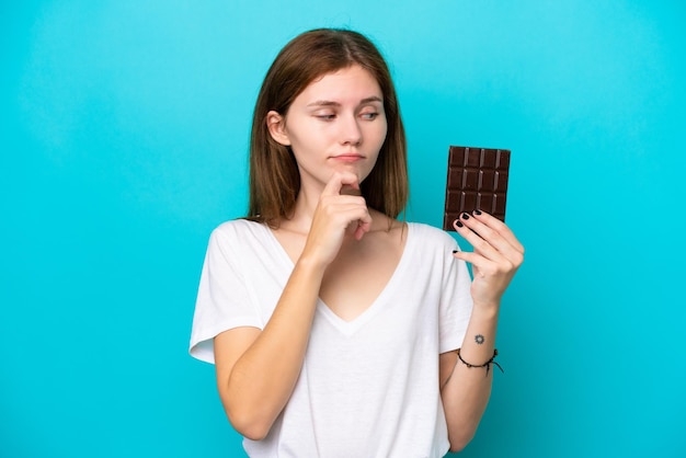 Giovane donna inglese con cioccolato isolato su sfondo blu con dubbi e pensare