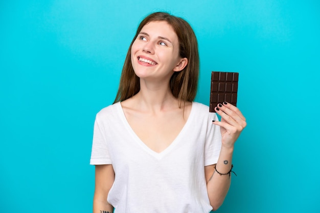 Молодая англичанка с шоколадом на синем фоне думает об идее, глядя вверх