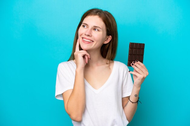 Young English woman with chocolat isolated on blue background thinking an idea while looking up