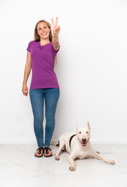 Young English woman with her dog isolated on white background smiling and showing victory sign