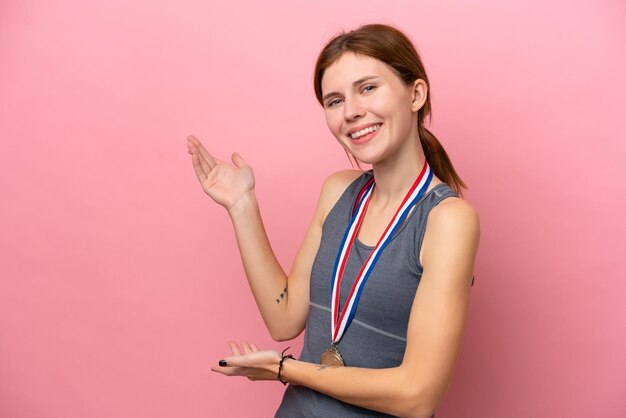 Young english woman with medals isolated on pink background\
extending hands to the side for inviting to come