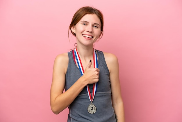 Young English woman with medals isolated on pink background giving a thumbs up gesture