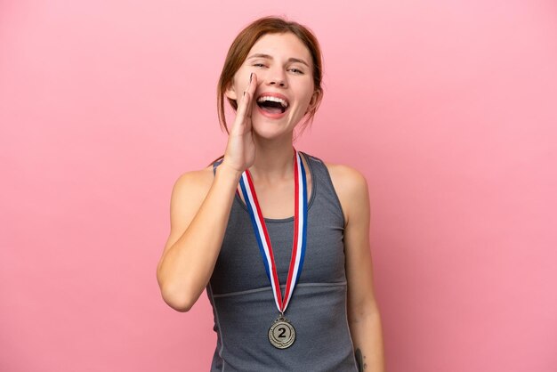 Photo young english woman with medals isolated on pink background shouting with mouth wide open