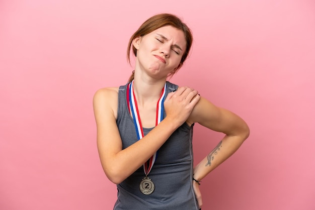 분홍색 배경에 격리된 메달을 가진 젊은 영국 여성은 노력한 것에 대해 어깨 통증으로 고통