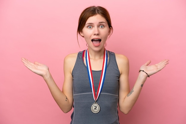 Young English woman with medals isolated on pink background with shocked facial expression