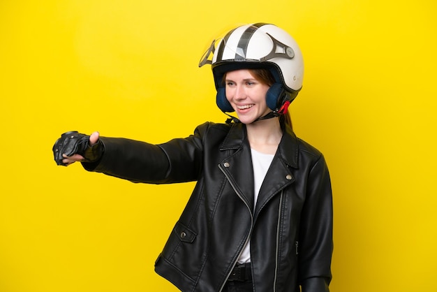 Молодая англичанка в мотоциклетном шлеме на желтом фоне показывает большой палец вверх