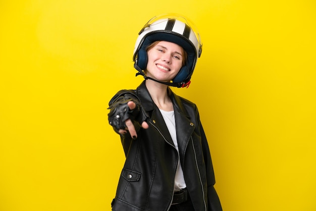 Young english woman with a motorcycle helmet isolated on yellow background pointing front with happy expression