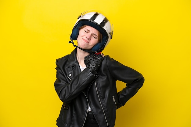 努力をしたために肩の痛みに苦しんで黄色の背景に分離されたオートバイのヘルメットを持つ若いイギリス人女性