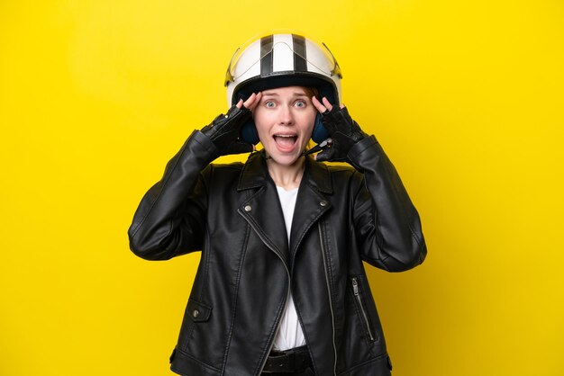 Young English woman with a motorcycle helmet isolated on yellow background with surprise expression