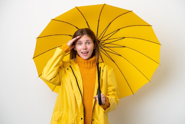 Young English woman with rainproof coat and umbrella isolated on white background with surprise expression