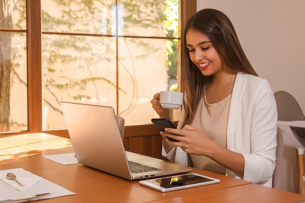 レストランでコーヒーを飲みながらスマートフォンで作業している若い進取の気性のある女の子。