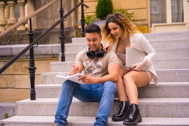 Young entrepreneur couple doing teamwork. In the city and with a computer, a boy in headphones and a girl in a white suit