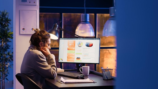 Young entrepreneur feeling sleepy in business office, working late on marketing strategy development. Startup manager yawning and being tired at job, planning financial statistics graphs.