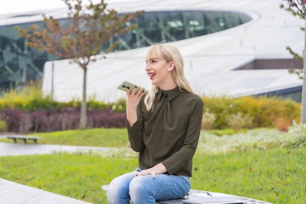 Young entrepreneur girl in a business park sending an audio note with the phone