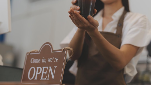 Photo young entrepreneur holding open sign on glass door at cafe