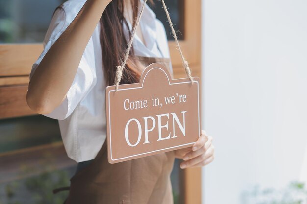 Photo young entrepreneur holding open sign on glass door at cafe