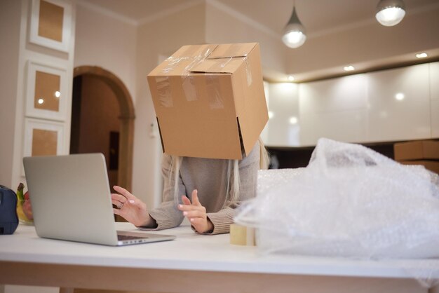 Young entrepreneur is holding cardboard boxes and place it on her head after successfully in sale products while sitting on comfortable the couch and working in living room at home office