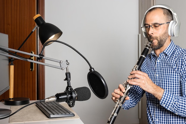 Young entrepreneur playing the clarinet at home and recording music to stream it online with his computer