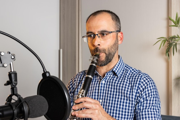 Giovane imprenditore che suona il clarinetto a casa e registra musica per trasmetterla in streaming online con il suo computer