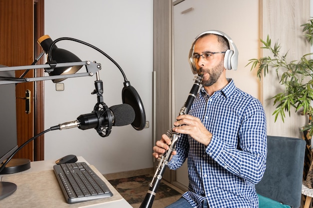 Фото Молодой предприниматель играет на кларнете дома и записывает музыку для потоковой передачи в интернете на своем компьютере.