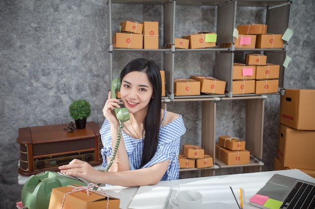Young entrepreneur talking on a phone as she sits at her desk in a home office.