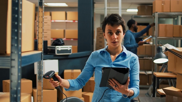 Молодой предприниматель использует сканер и планшет для инвентаризации, сканируя штрих-коды с упаковок на складских полках. Женщина проверяет запасы товаров в коробках, логистика цепочки поставок.