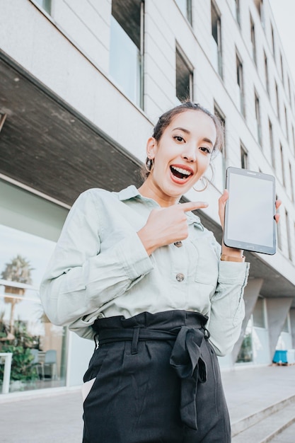 Young entrepreneur woman holding a tablet showing the blank screen to camera, copy space, office and business concept, copy space, outdoors, well dressed